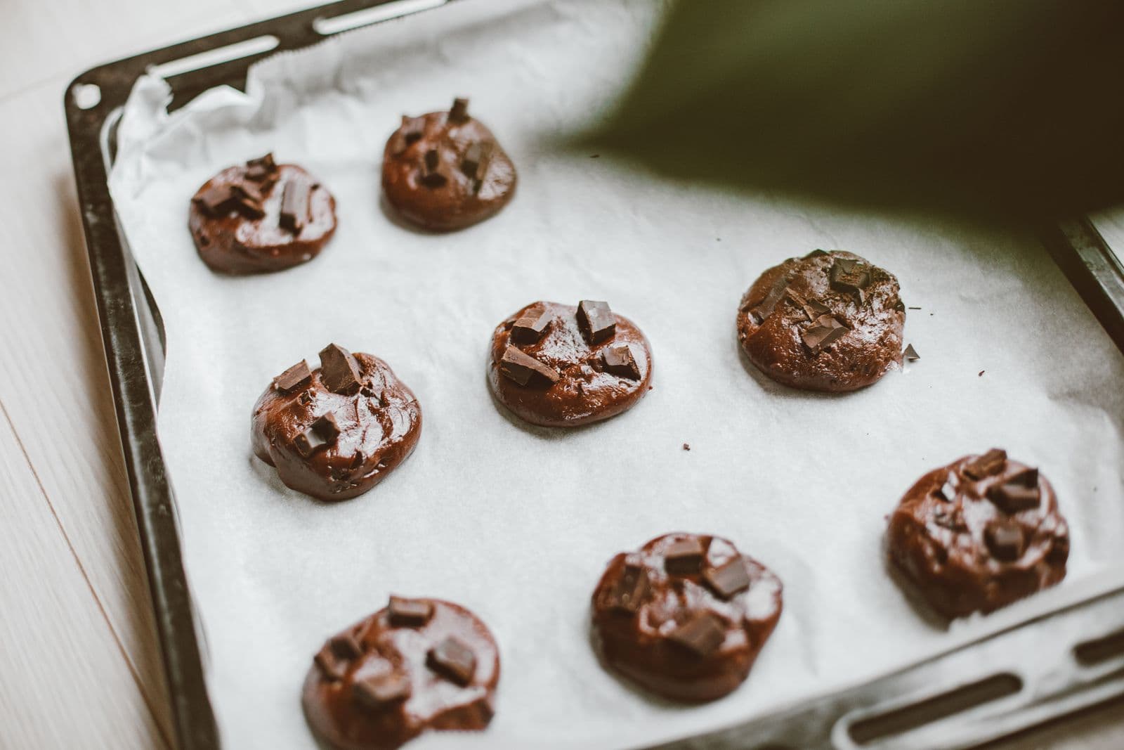 Cookies de chocolate crus, já moldados e achatados sobre papel manteiga na assadeira
