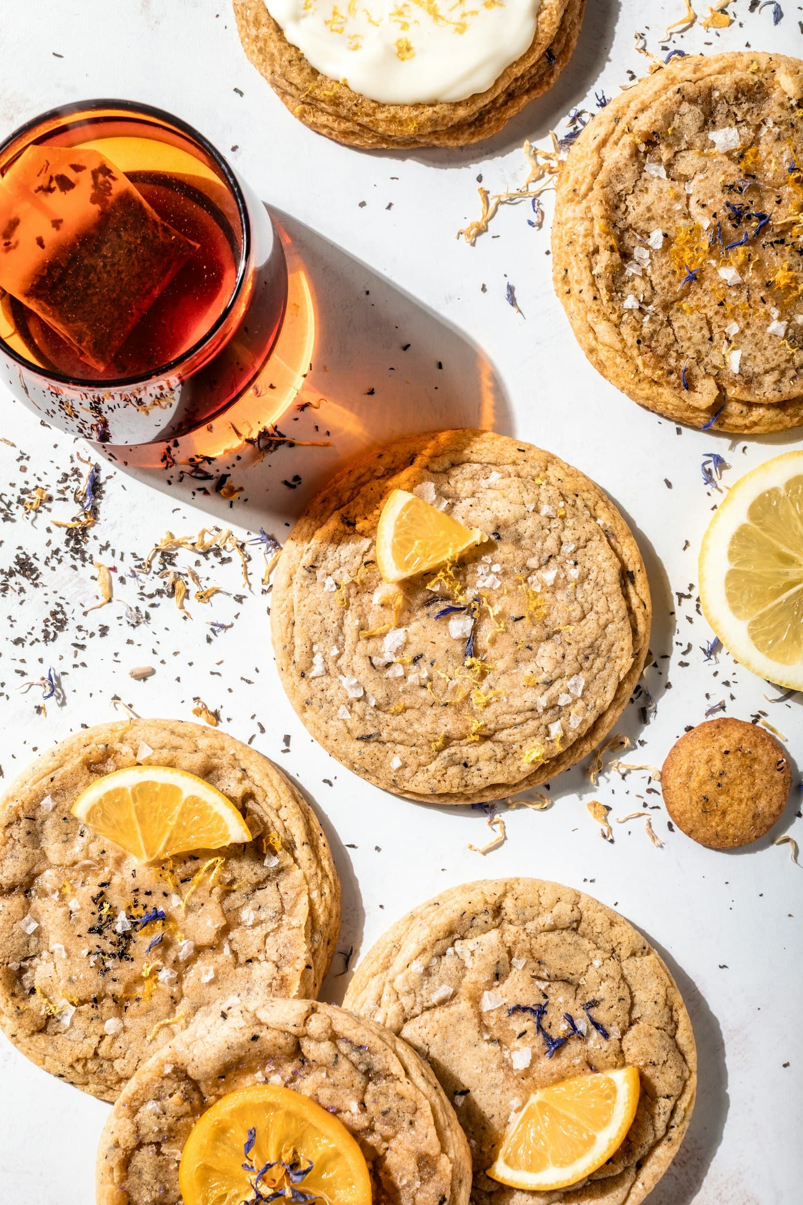 Cookies com limão e flores secas ao lado de um copo de chá, vistos de cima
