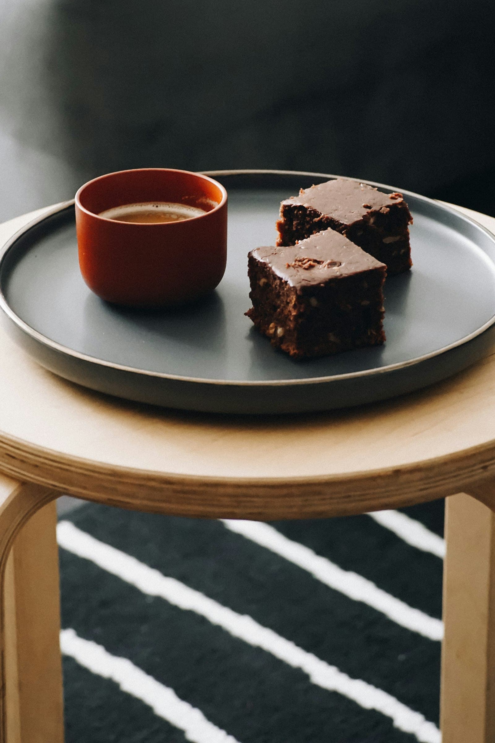 Dois brownies em prato cinza-escuro ao lado de um copinho de café terracota
