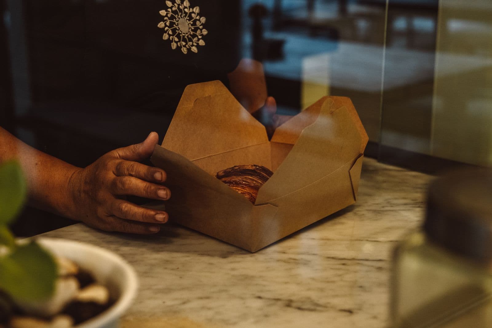 Mão colocando um pão em uma caixa de papel kraft
