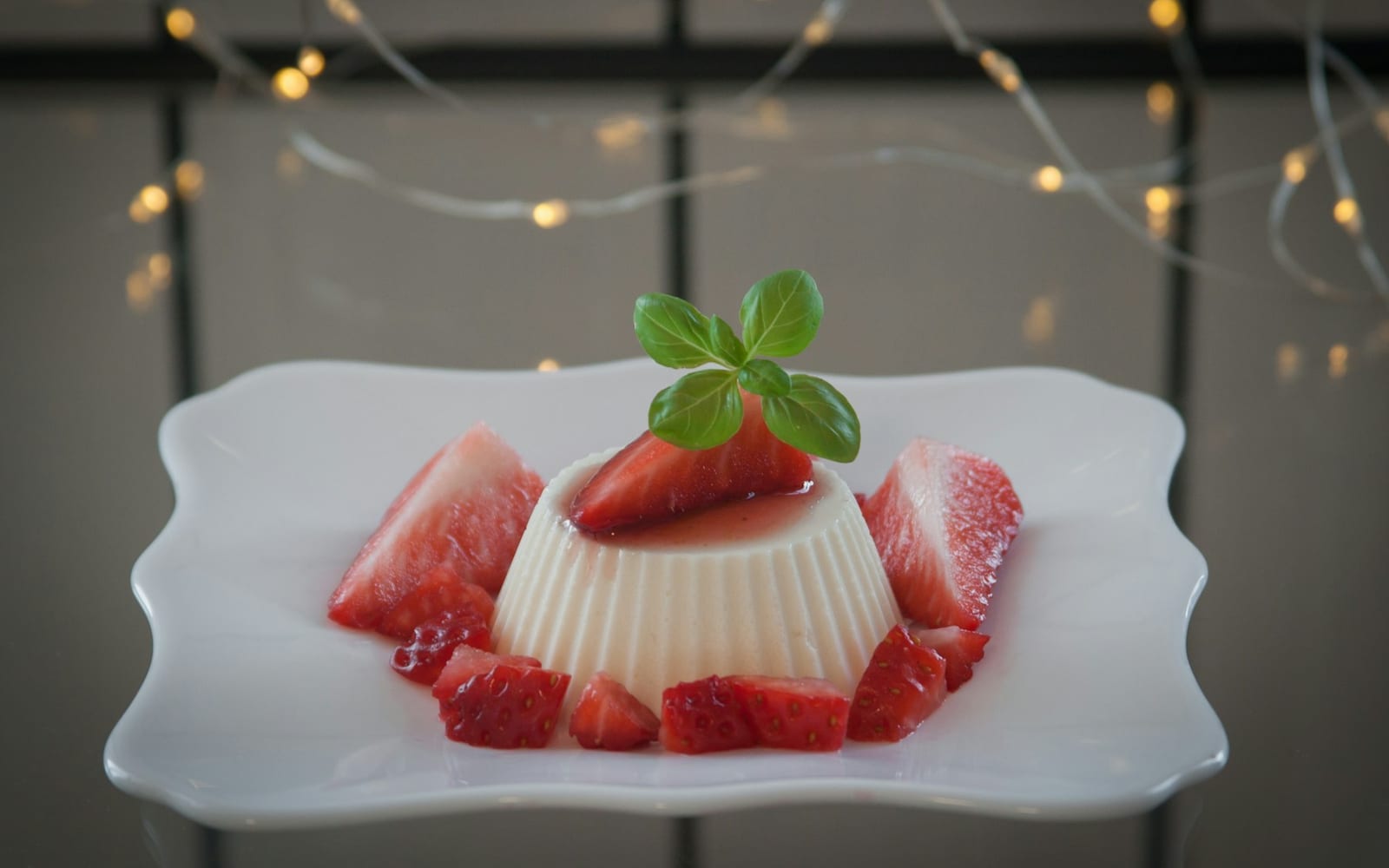 Sobremesa cremosa desenformada sobre um prato branco, decorada com morangos e uma folha de hortelã