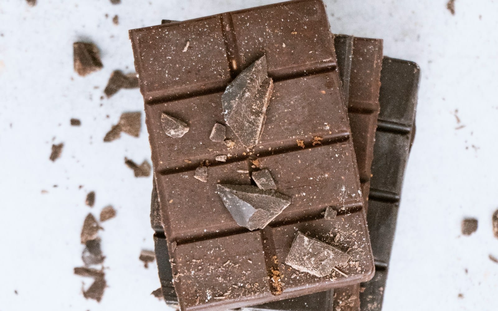 Pilha de barras de chocolate escuro com lascas espalhadas sobre uma superfície clara